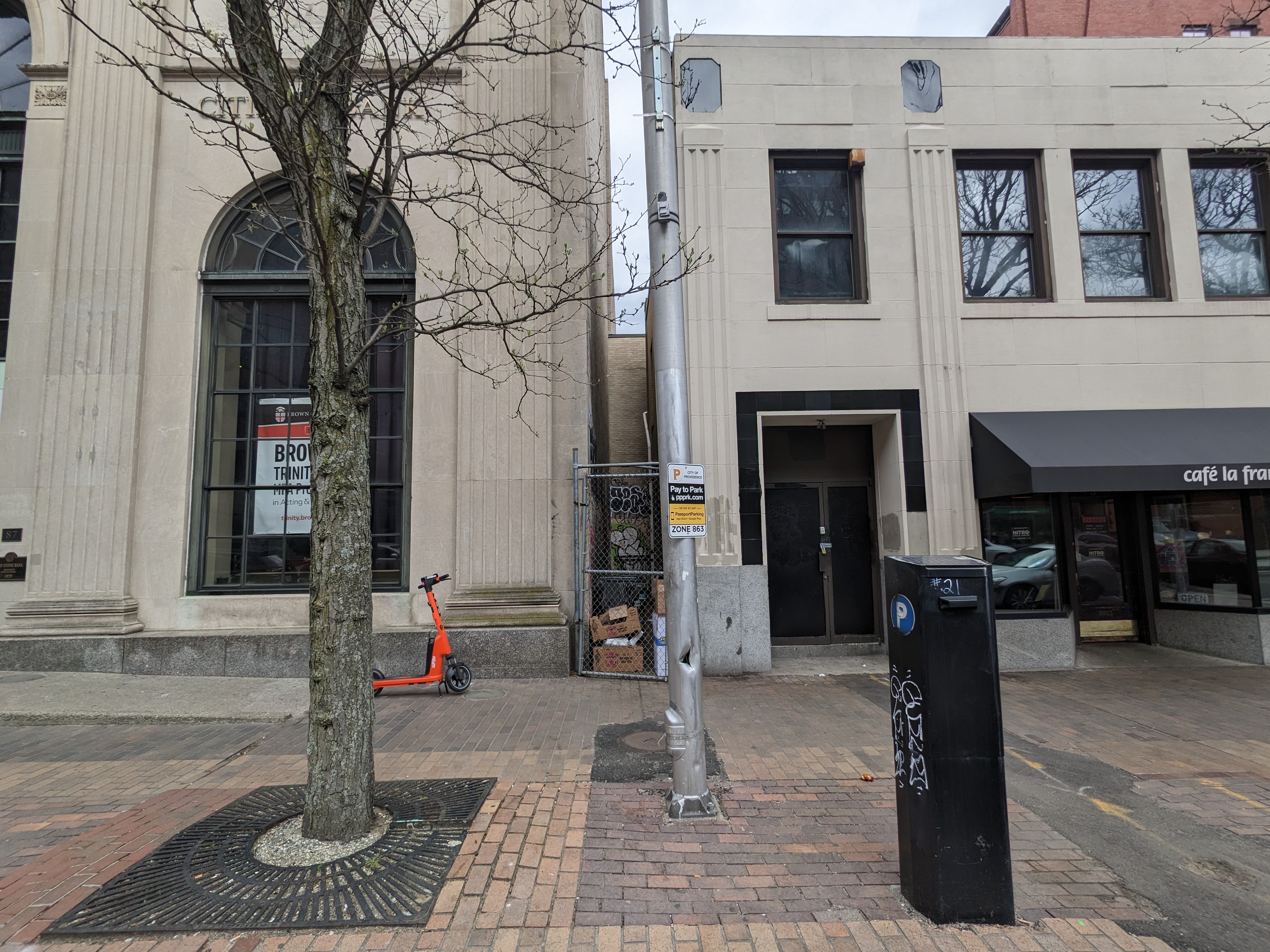 A photograph of a sidewalk with two storefronts, a tree, and a parking meter
