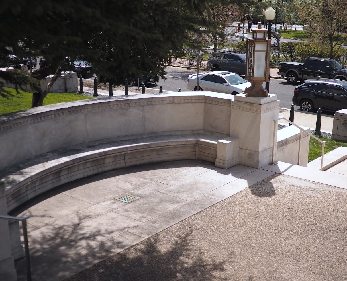 A photograph of a curved marble bench under a tree